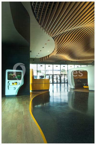 Intérieur moderne avec plafond ondulé en bois, sol mixte bois et noir, guichet automatique et espaces arrondis.