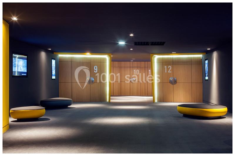 Couloir moderne avec éclairage tamisé, portes numérotées en bois et sièges ronds jaunes et noirs au premier plan.