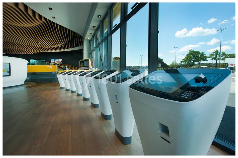 File d'écrans tactiles modernes alignés dans un espace lumineux avec de grandes baies vitrées donnant sur l'extérieur.