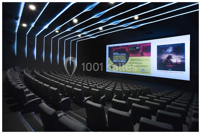 Salle de cinéma moderne avec sièges noirs alignés et grand écran affichant des bandes-annonces.