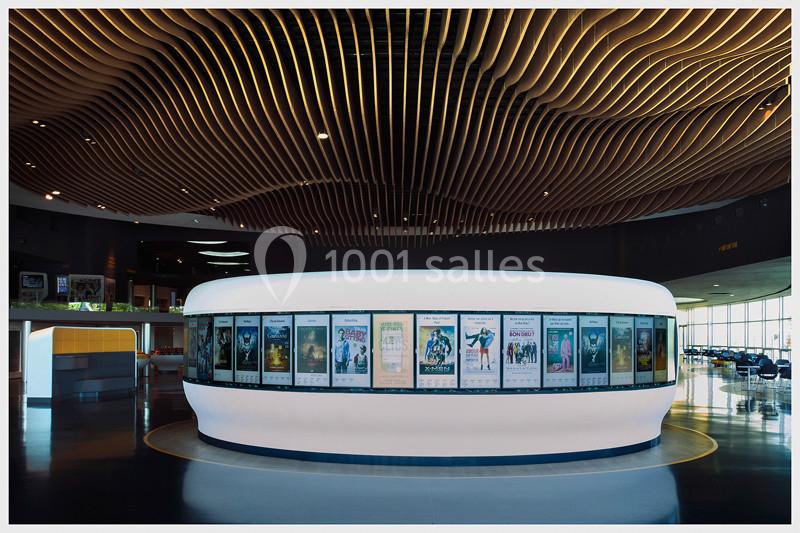 Mur circulaire lumineux affichant des posters de films dans un hall moderne avec un plafond ondulé en bois.