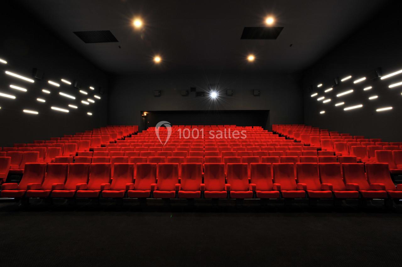 Salle de cinéma vide avec des rangées de sièges rouges et un éclairage tamisé.