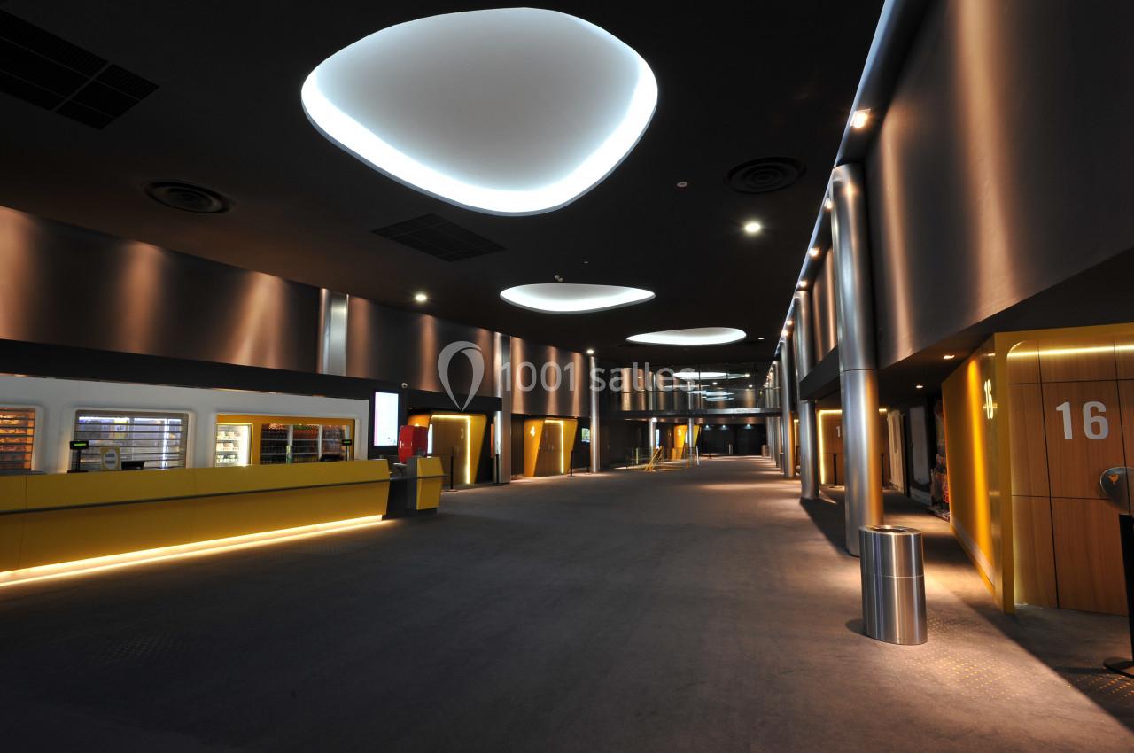 Hall moderne d'un cinéma avec éclairage design, comptoir de confiserie à gauche et numéros de salles visibles à droite.