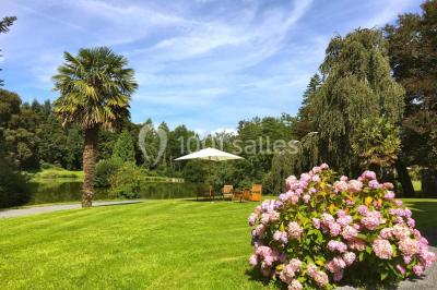 Statue blanche en forme de figure humaine tenant une vasque d'où s'écoule de l'eau, entourée de végétation.