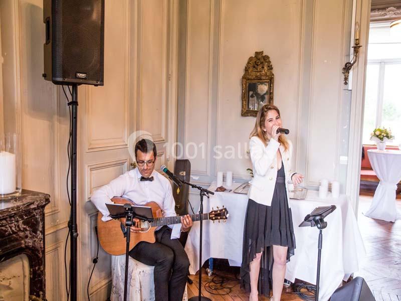 Un musicien jouant de la guitare et une chanteuse interprétant une chanson dans une salle élégante.