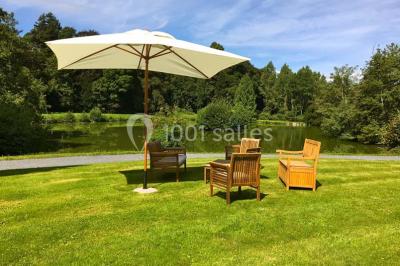 Statue blanche en forme de figure humaine tenant une vasque d'où s'écoule de l'eau, entourée de végétation.
