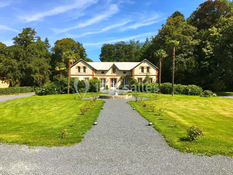 Allée gravillonnée menant à une maison en pierre entourée de pelouses et d'arbres sous un ciel bleu.