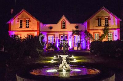 Statue blanche en forme de figure humaine tenant une vasque d'où s'écoule de l'eau, entourée de végétation.