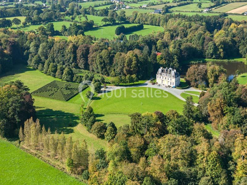 Vue aérienne d'un château entouré de vastes pelouses, d'arbres et de jardins dans un paysage rural verdoyant.