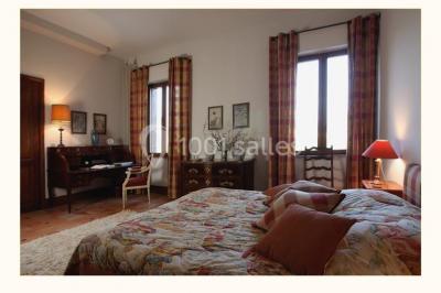 Chambre lumineuse avec lit double, bureau en bois, lampes allumées et rideaux à carreaux devant des fenêtres.