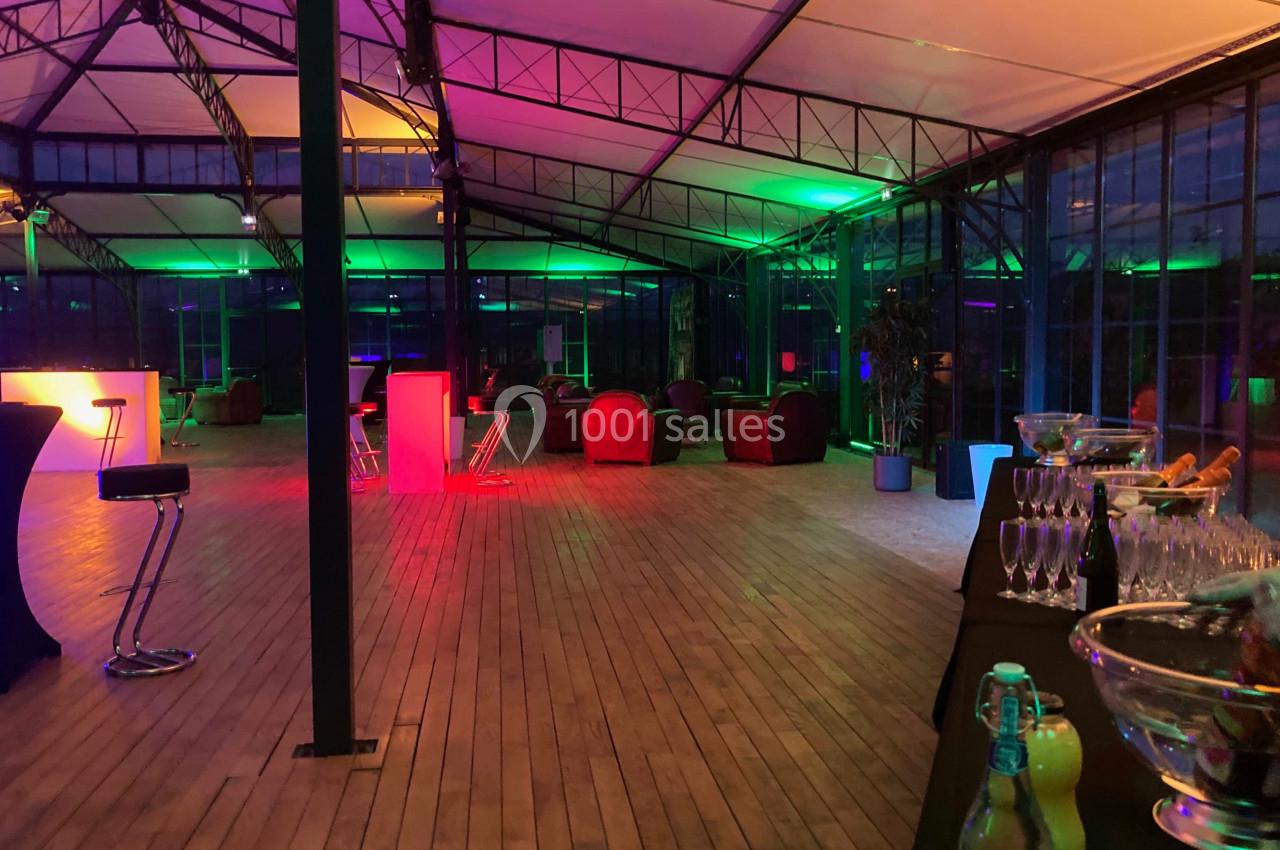 Salle avec parquet, mobilier lounge et éclairage coloré, préparée pour un événement avec buffet et boissons.