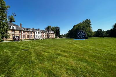 Chambre lumineuse avec lit double, bureau en bois, lampes allumées et rideaux à carreaux devant des fenêtres.