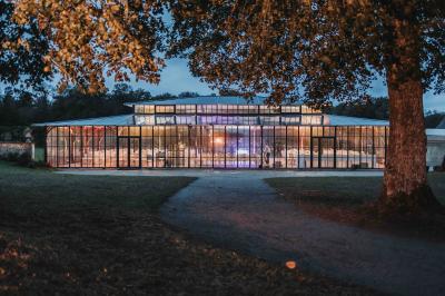 Chambre lumineuse avec lit double, bureau en bois, lampes allumées et rideaux à carreaux devant des fenêtres.
