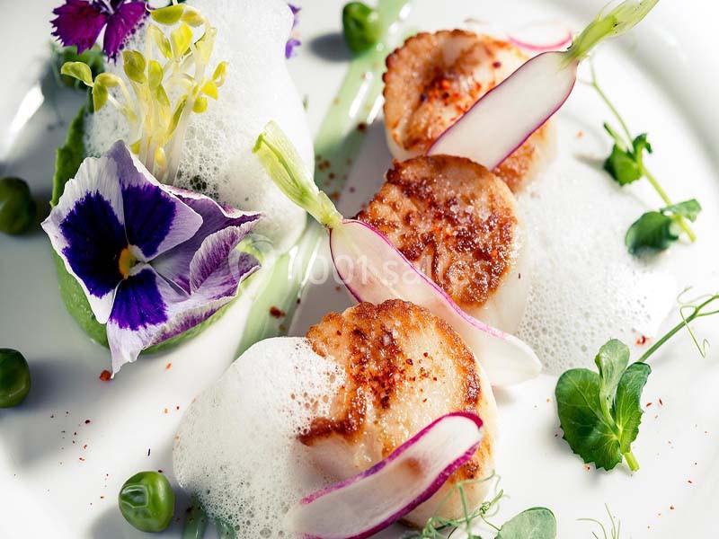 Noix de Saint-Jacques poêlées servies avec mousse légère, radis, fleurs comestibles et purée verte.