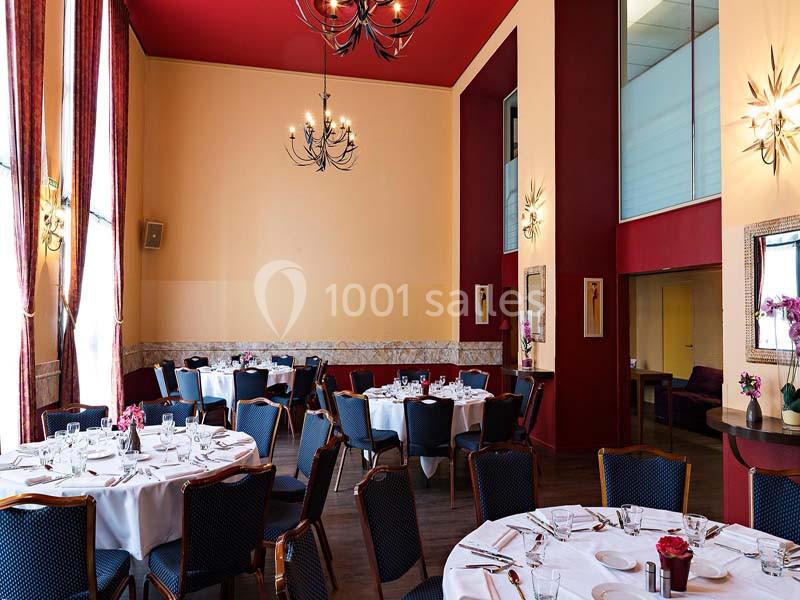 Salle de réception élégante avec tables rondes dressées, chaises noires et décorations murales dans des tons rouges et…