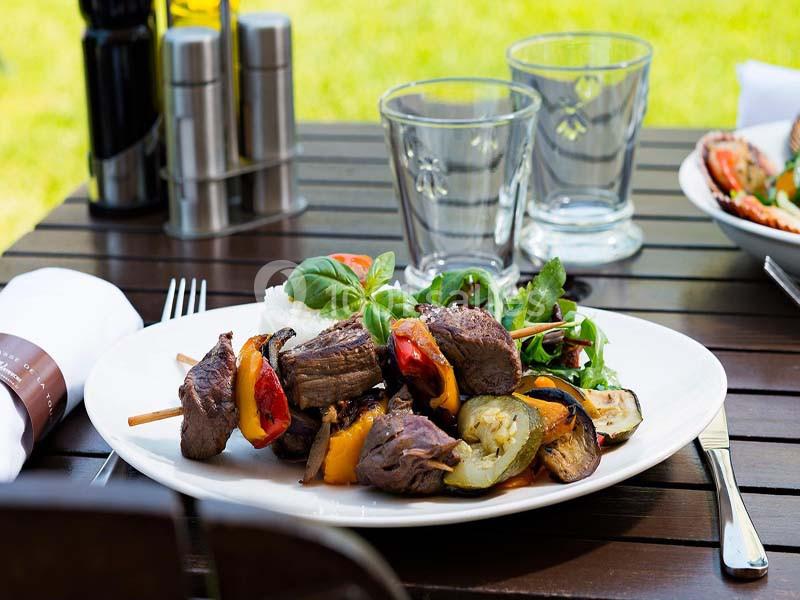 Assiette de brochettes de viande grillée avec légumes, accompagnée de salade verte, servie sur une table en extérieur.