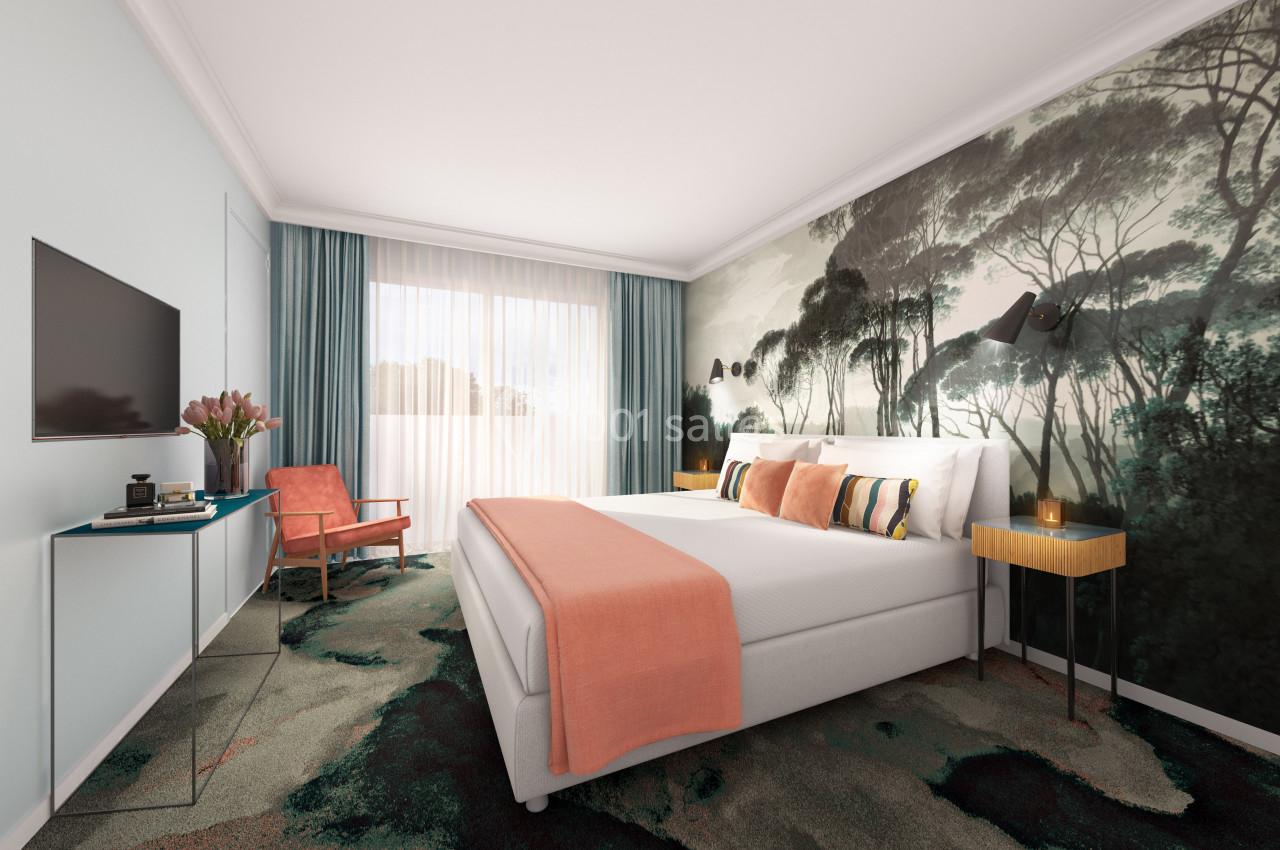 Chambre lumineuse avec un lit double, un mur décoré de motifs forestiers, un fauteuil et une grande fenêtre avec rideaux.