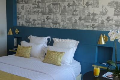 Lit double avec oreillers et coussins jaunes, éclairé par des lampes dorées, devant un mur décoré de motifs artistiques.