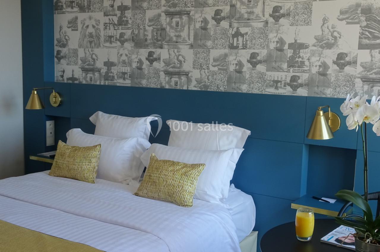 Lit double avec oreillers et coussins jaunes, éclairé par des lampes dorées, devant un mur décoré de motifs artistiques.