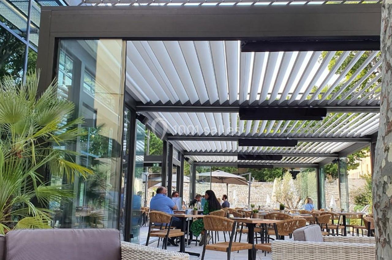 Terrasse extérieure moderne avec pergola à lames orientables, tables et chaises occupées par des clients.