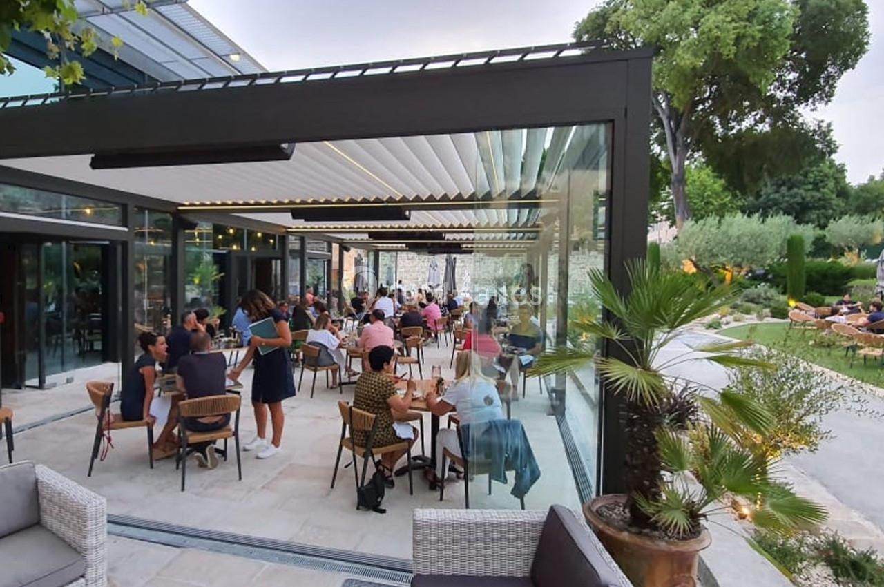 Terrasse couverte d’un restaurant avec des clients attablés, entourée de végétation et éclairée par la lumière naturelle.