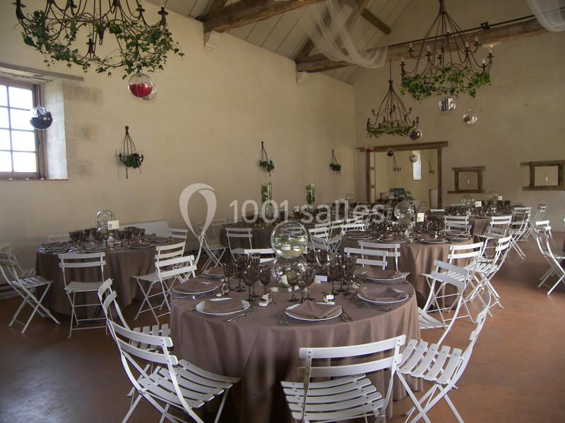 Salle de réception décorée avec des tables rondes dressées, chaises blanches pliantes et suspensions végétales.