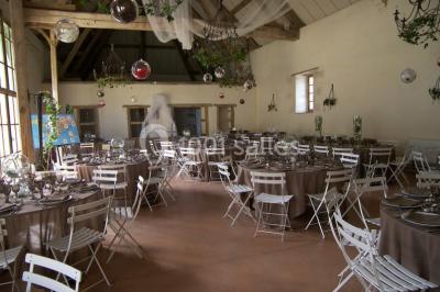 Salle lumineuse avec cuisine ouverte, murs rouges, poutres apparentes, mobilier en bois et fauteuils en osier.