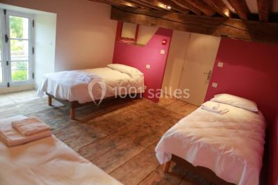 Salle lumineuse avec cuisine ouverte, murs rouges, poutres apparentes, mobilier en bois et fauteuils en osier.