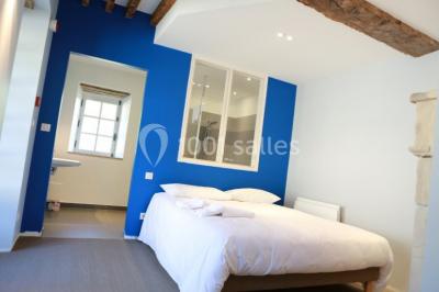 Salle lumineuse avec cuisine ouverte, murs rouges, poutres apparentes, mobilier en bois et fauteuils en osier.