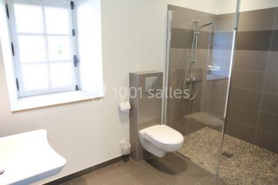 Salle lumineuse avec cuisine ouverte, murs rouges, poutres apparentes, mobilier en bois et fauteuils en osier.