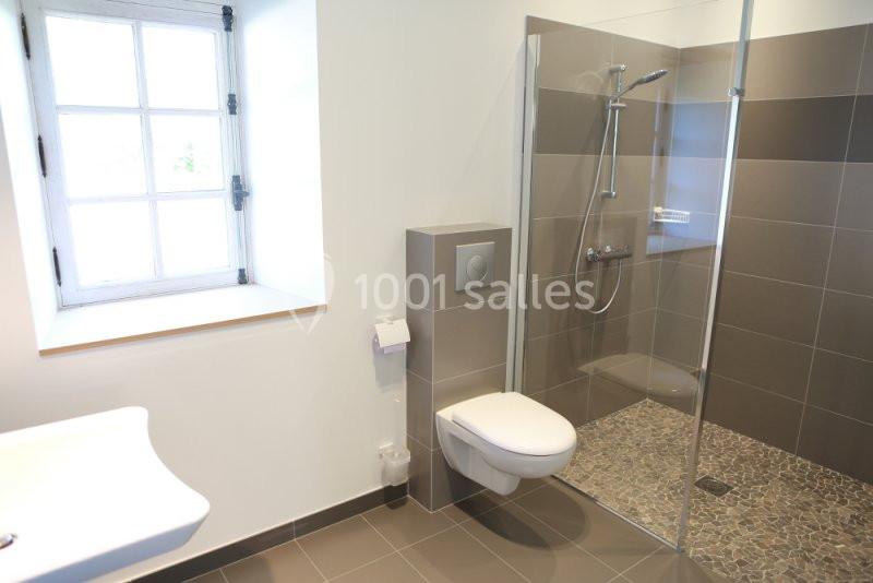 Salle de bain moderne avec douche à l'italienne, toilettes suspendues et fenêtre à carreaux.