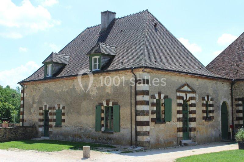 Maison en pierre avec des volets verts, toit en pente et détails de briques décoratives, sous un ciel bleu.