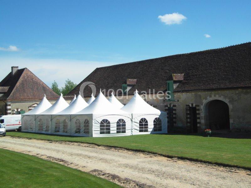 Tente blanche avec fenêtres installée sur une pelouse près d'un bâtiment ancien en pierre sous un ciel dégagé.