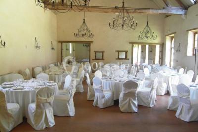 Salle lumineuse avec cuisine ouverte, murs rouges, poutres apparentes, mobilier en bois et fauteuils en osier.