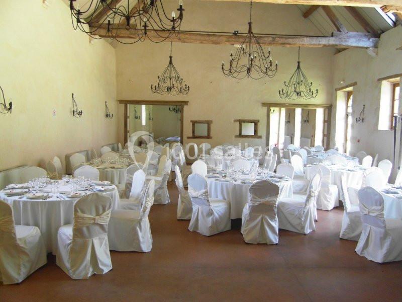 Salle de réception lumineuse avec tables rondes dressées et chaises blanches sous des lustres en fer forgé.