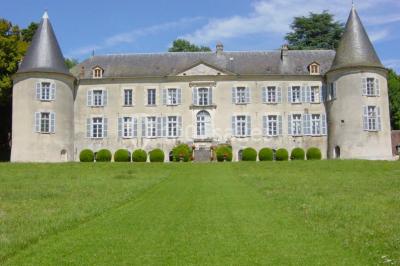 Salle lumineuse avec cuisine ouverte, murs rouges, poutres apparentes, mobilier en bois et fauteuils en osier.