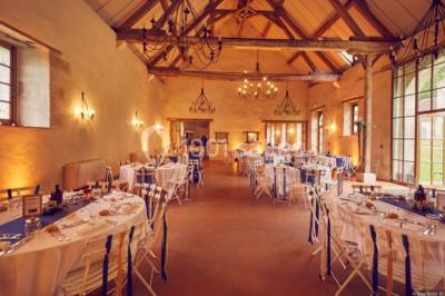 Salle lumineuse avec cuisine ouverte, murs rouges, poutres apparentes, mobilier en bois et fauteuils en osier.