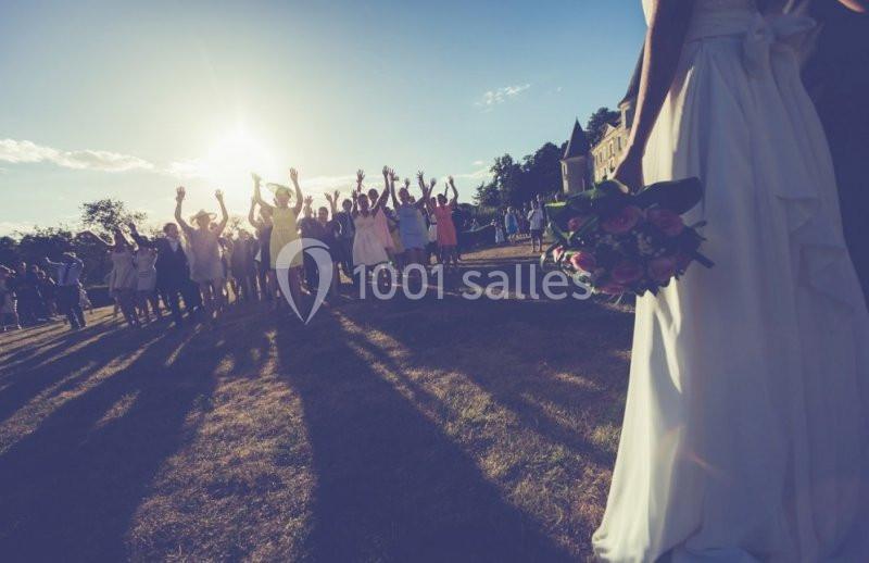 Une mariée tenant un bouquet regarde un groupe de personnes levant les bras sur une pelouse au coucher du soleil.