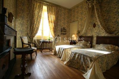 Salle lumineuse avec cuisine ouverte, murs rouges, poutres apparentes, mobilier en bois et fauteuils en osier.