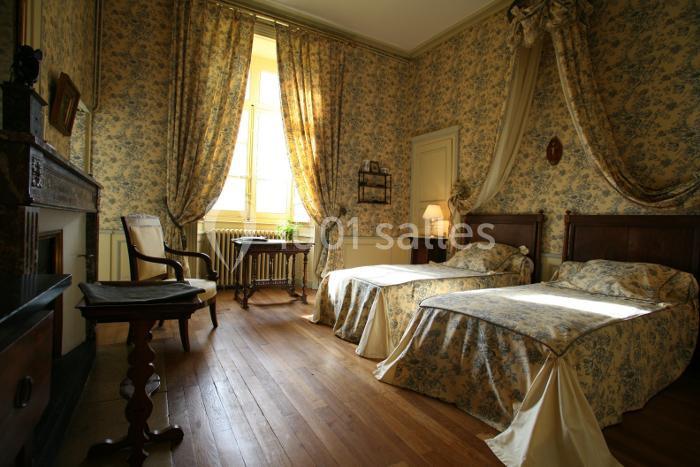 Chambre ancienne avec deux lits simples, décorée de motifs floraux, parquet en bois et lumière naturelle.