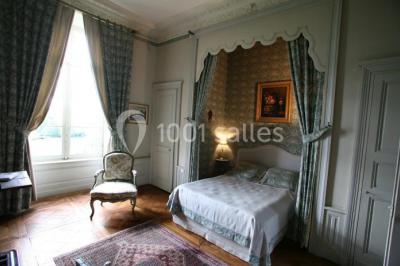 Salle lumineuse avec cuisine ouverte, murs rouges, poutres apparentes, mobilier en bois et fauteuils en osier.