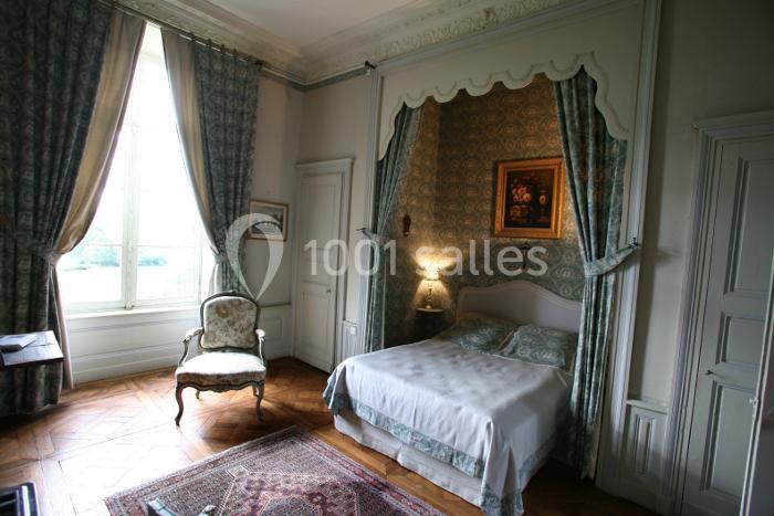Chambre élégante avec lit à baldaquin, fauteuil ancien, tapis et grande fenêtre laissant entrer la lumière naturelle.