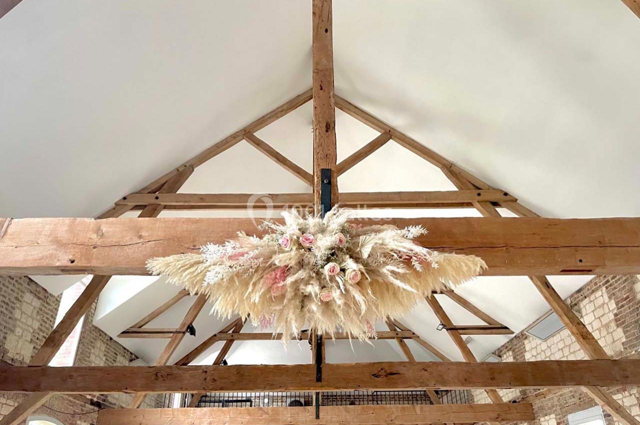 Décoration florale suspendue avec des pampas et des fleurs séchées, accrochée à une poutre en bois dans une pièce lumineuse.