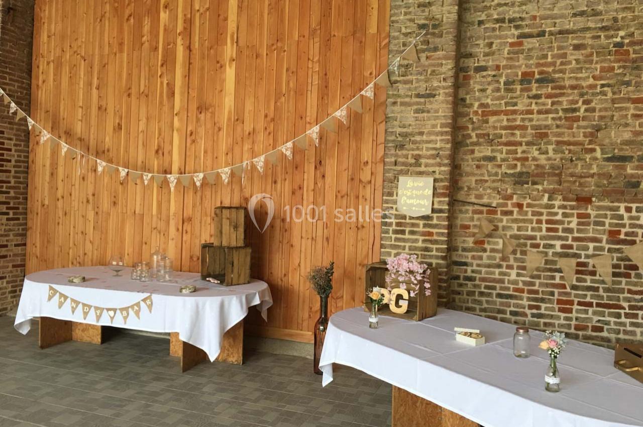 Salle décorée pour un événement avec des tables recouvertes de nappes blanches, guirlandes et éléments rustiques en bois.