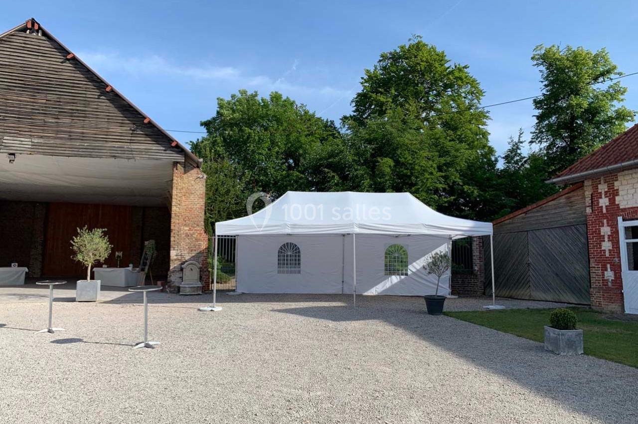 Tente blanche installée sur un sol gravillonné, entourée de bâtiments en briques et de verdure.