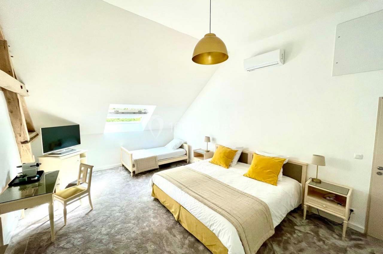 Chambre lumineuse avec lit double, lit simple, bureau, télévision, climatisation et décoration aux tons clairs et jaunes.