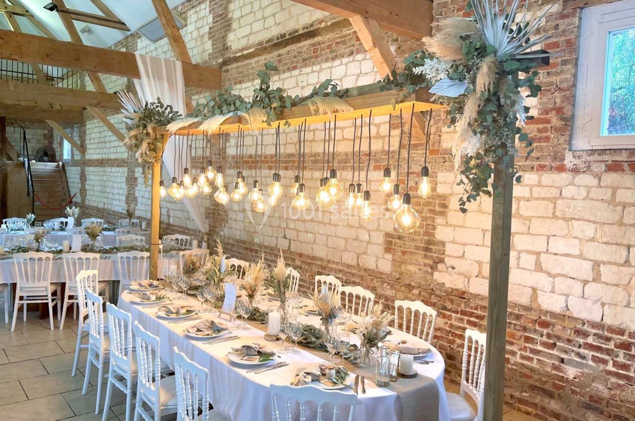 Table décorée pour un repas festif dans une salle en briques avec guirlande d'ampoules suspendues et fleurs séchées.