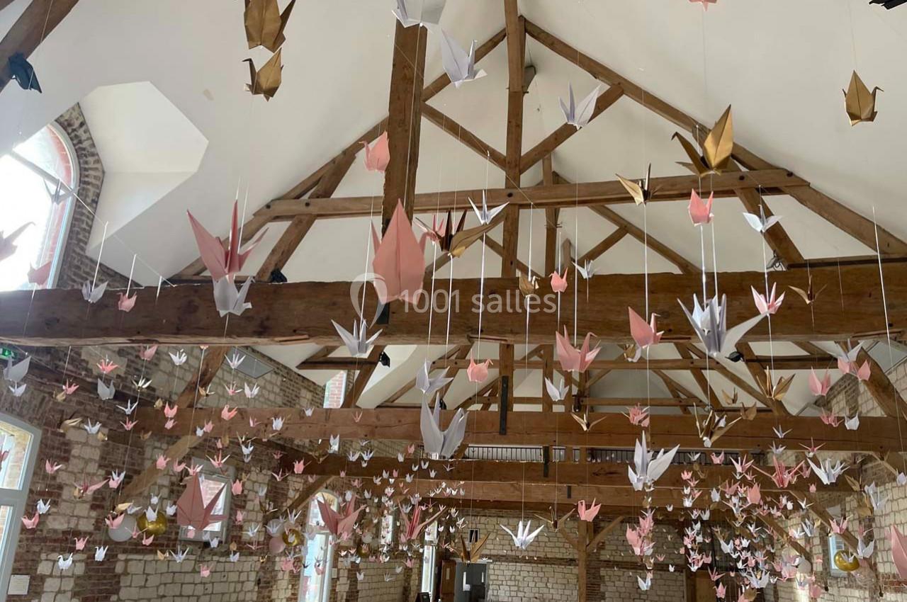Origamis de grues suspendus au plafond d'une salle avec charpente en bois et murs en briques apparentes.