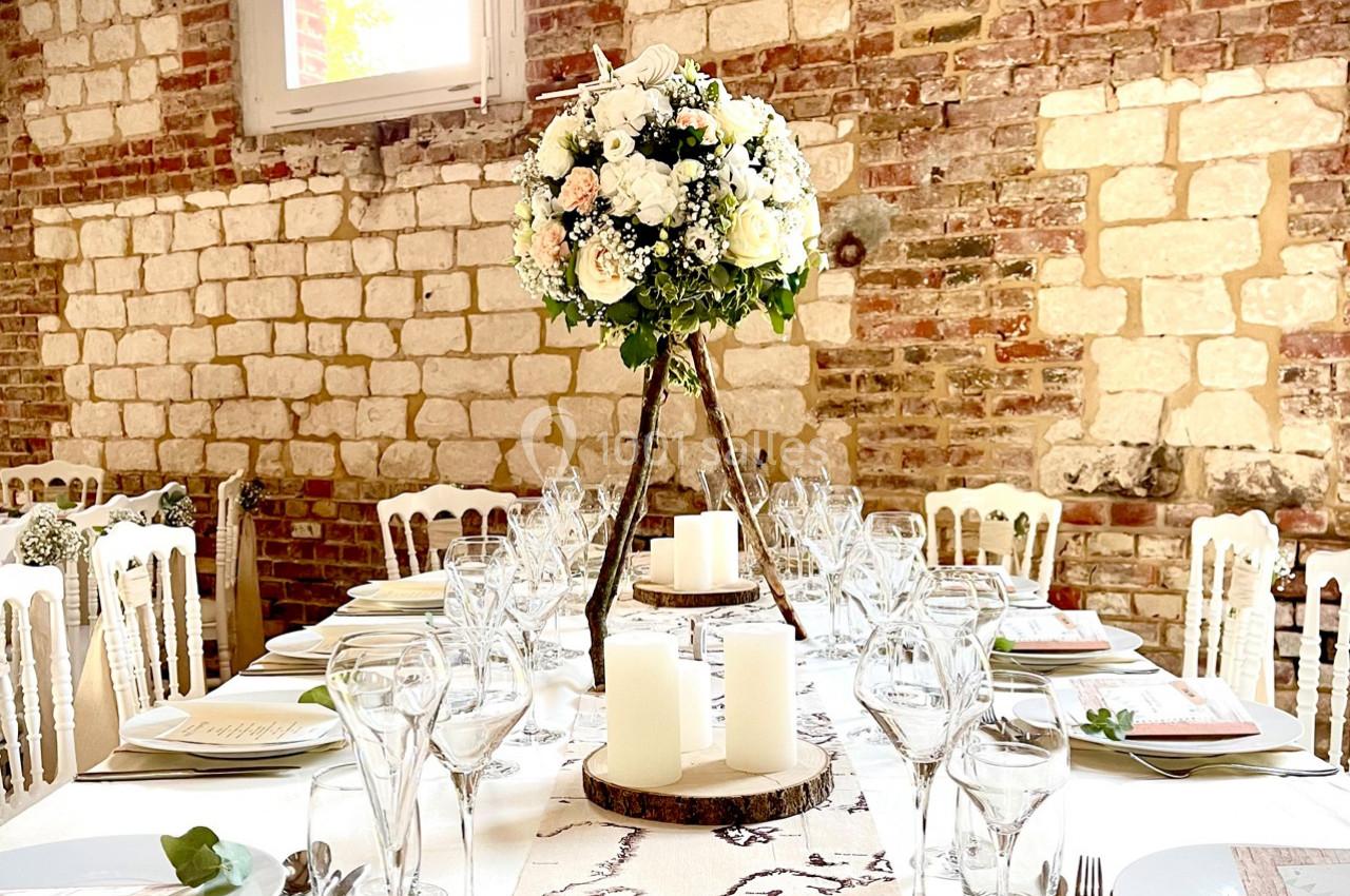 Table de réception élégamment dressée avec des verres, des assiettes, des bougies et un centre de table floral sur pied.