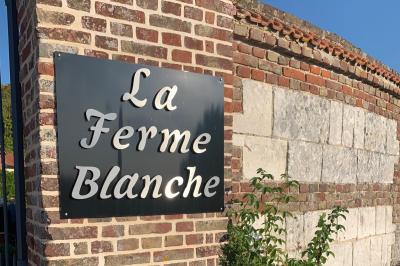 Panneau en métal avec l'inscription ’La Ferme Blanche’, reflétant la lumière du soleil couchant.
